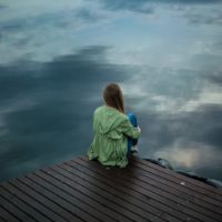 woman in green jacket sitting on dock