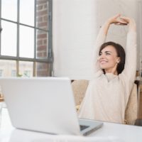 woman smiling and taking a break from office work while sitting by her office table and stretching her arms