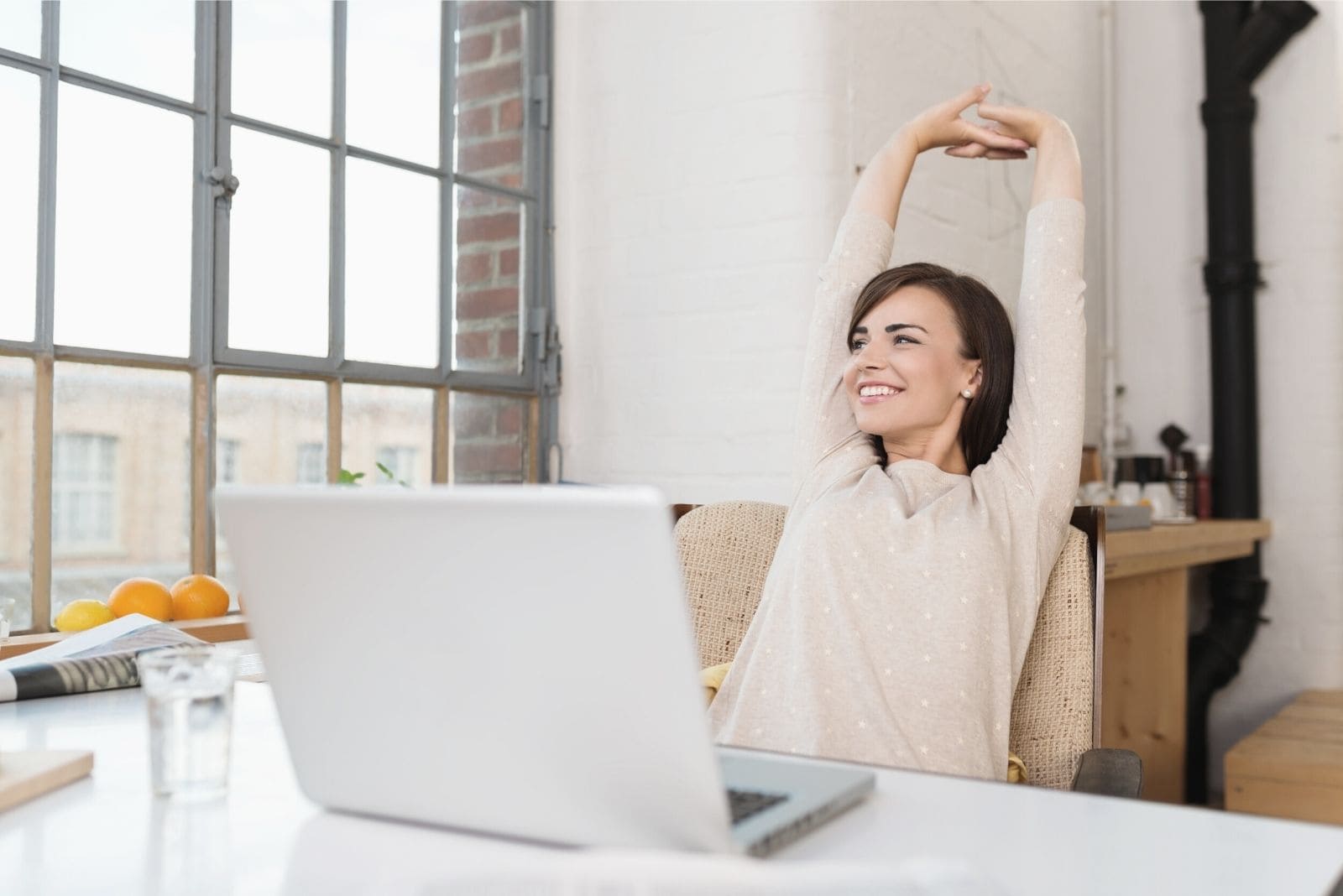 woman smiling and taking a break from office work while sitting by her office table and stretching her arms