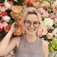 mujer con gafas de pie cerca de flores pétalos sonriendo