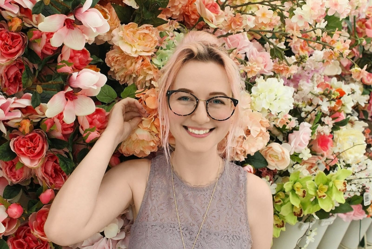 woman with eyeglasses standing near petaled flowers smiling