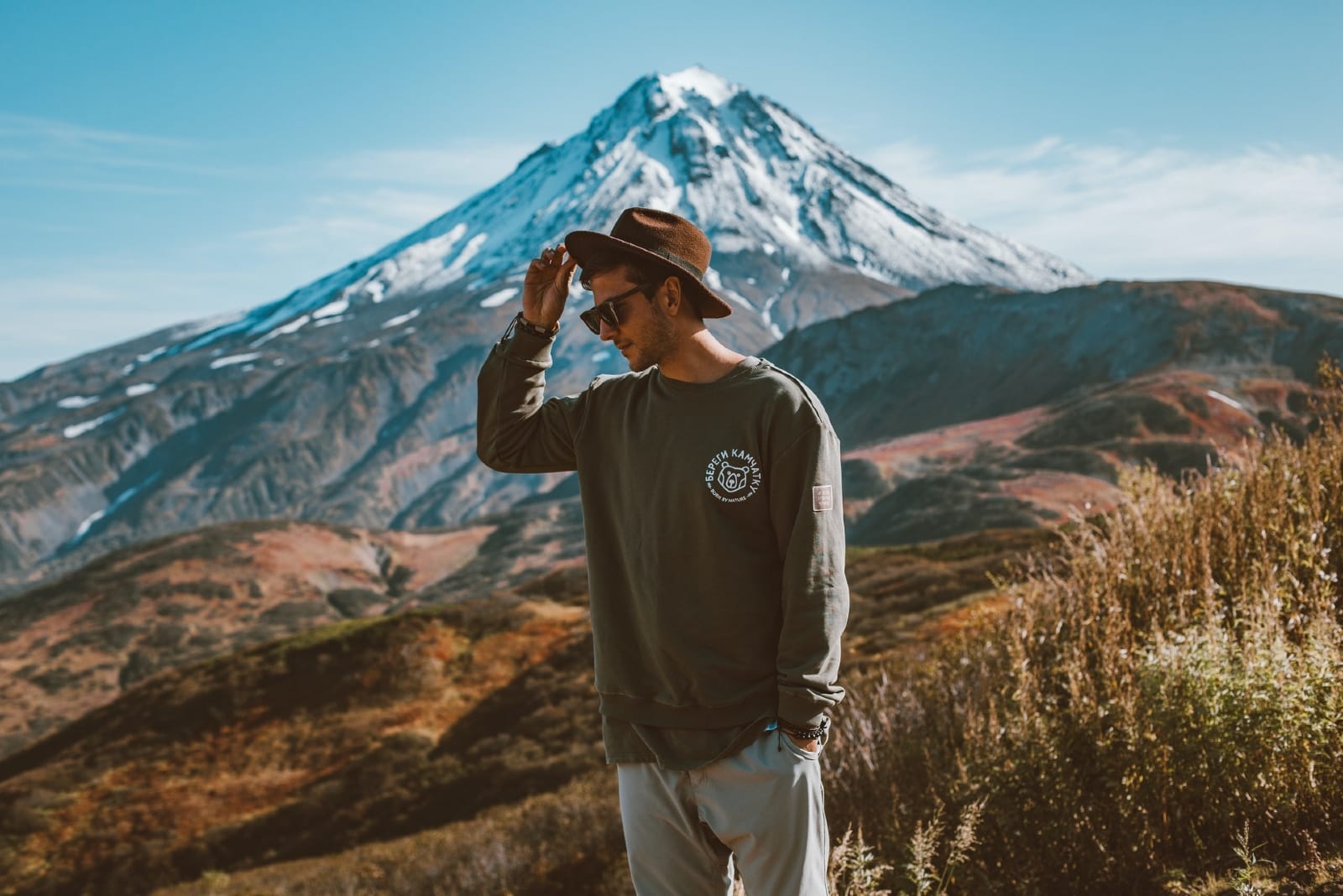 man holding hat while standing near mountain