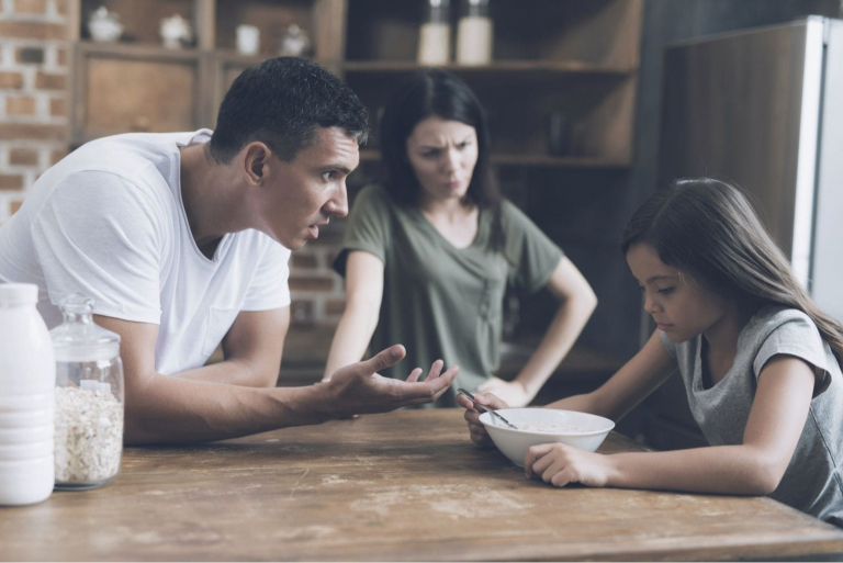 child scolded by parents during her meal in the table
