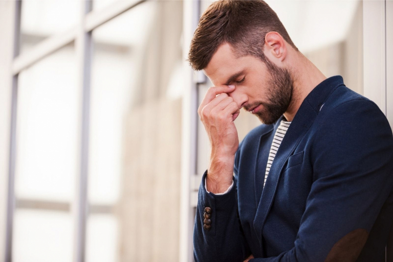 sad man holding her head leaning on the building's wall