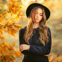woman wearing black dress and hat standing with arms crossed in the autumn park thinking deeply