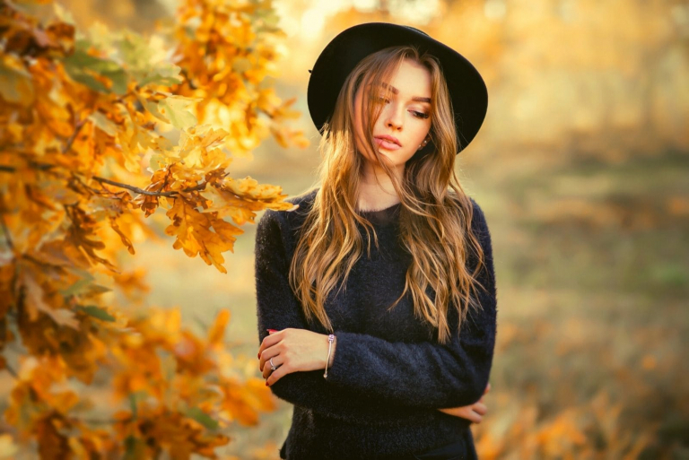 woman wearing black dress and hat standing with arms crossed in the autumn park thinking deeply