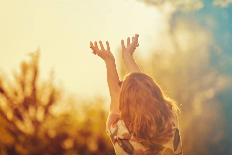 rear view of a woman praying for good weather in nature raising her hands facing the skies