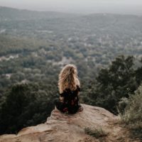 blonde woman sitting on cliff during sunset