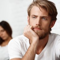 um jovem perturbado que apoia a cabeça com o punho cerrado e uma mulher triste nas suas costas, numa fotografia com rebarbas