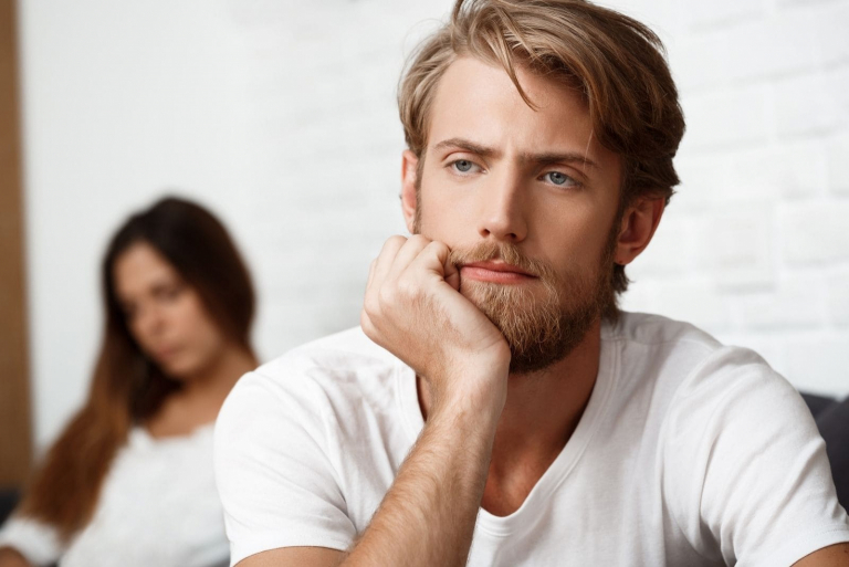 upset young man supporting his head with clenched fist with a sad woman at his back in burred photography