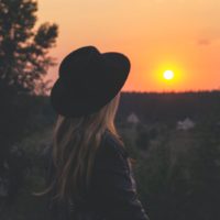 woman with black hat looking at sunset