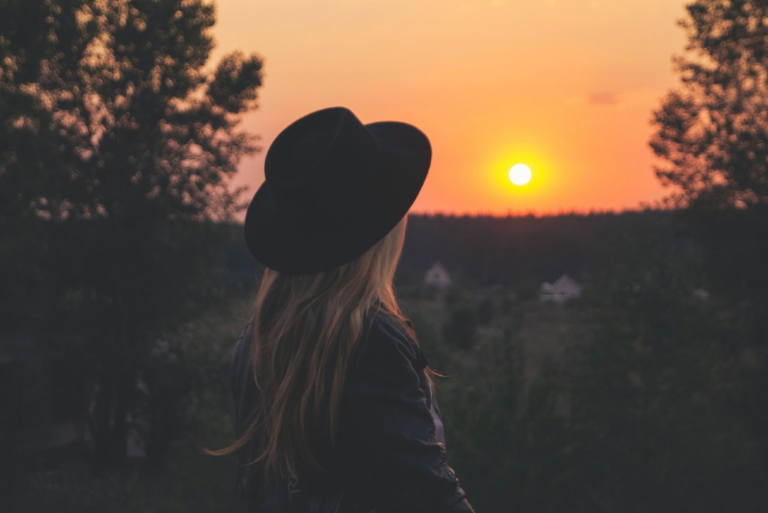 mulher com chapéu preto a olhar para o pôr do sol