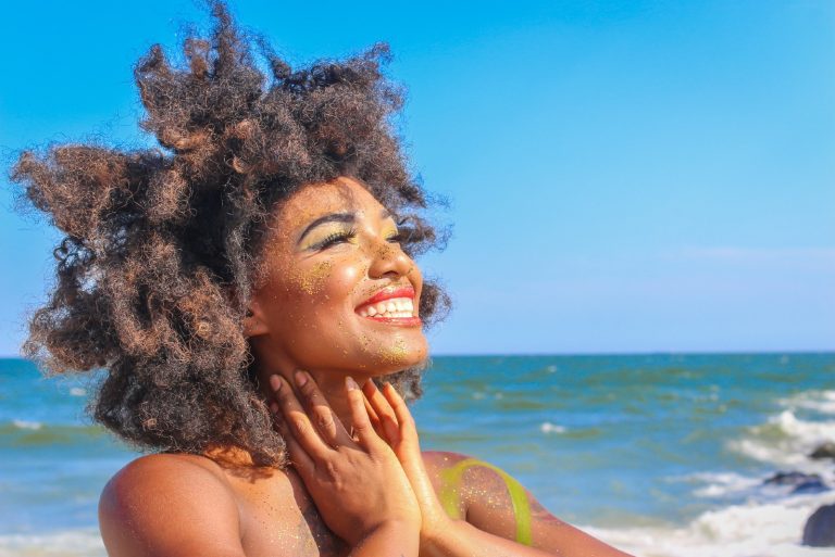 happpy woman with curly hair standing near sea