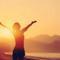 a determined strong woman standing on the beach with her arms outstretched at sunset