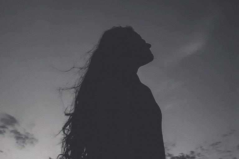 silhouette of a young woman standing outdoors looking up the sky in the night in a low angle