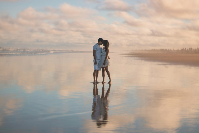 man and woman standing in shallow water during sunset