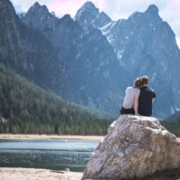 man and woman sitting on rock looking at mountain