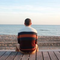 uomo seduto su un pannello di legno che guarda l'oceano