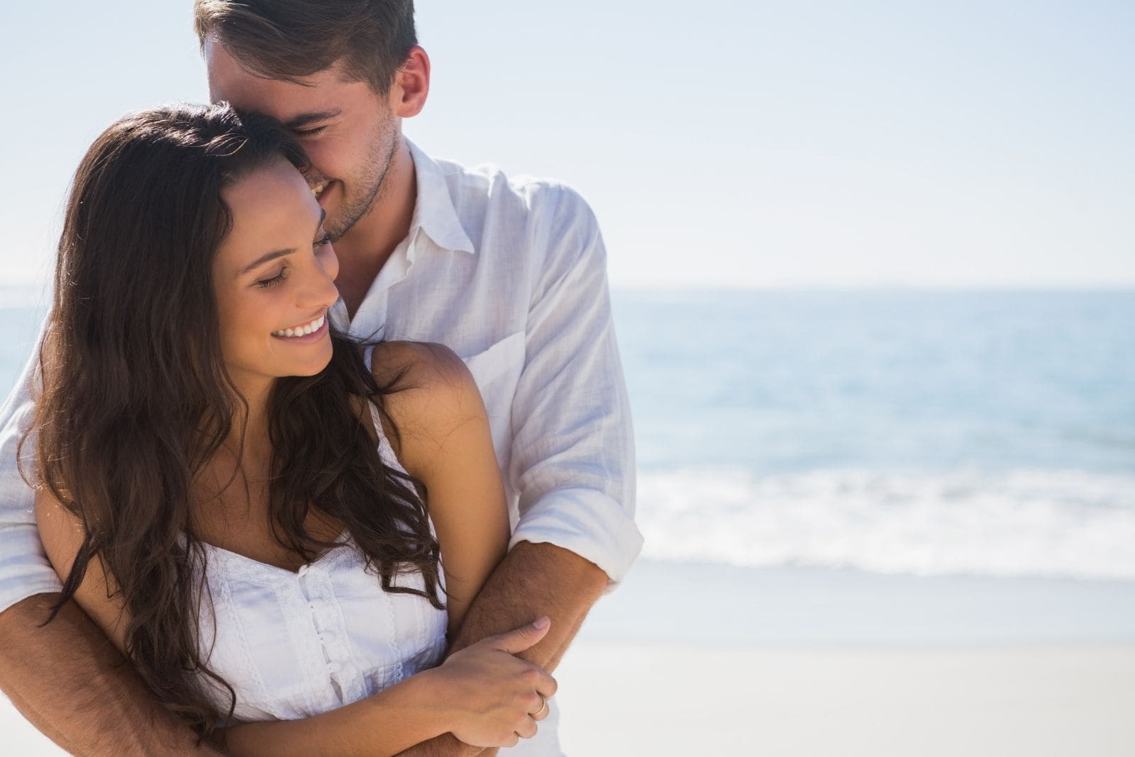 attractive couple cuddling sweetly in the beach wearing white top/dress