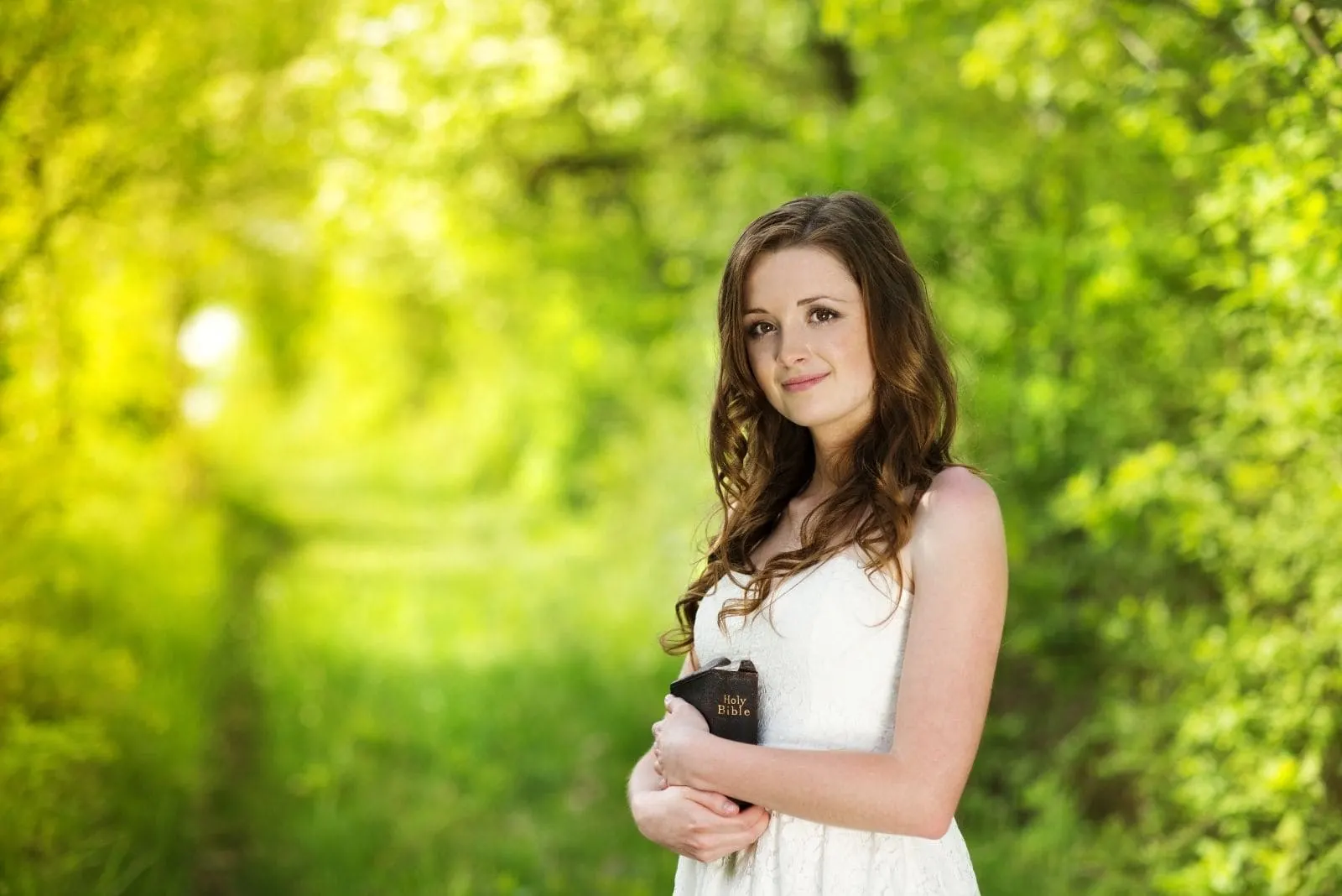 beautiful woman with a bible smiling and standing in the green garden wearing a dress