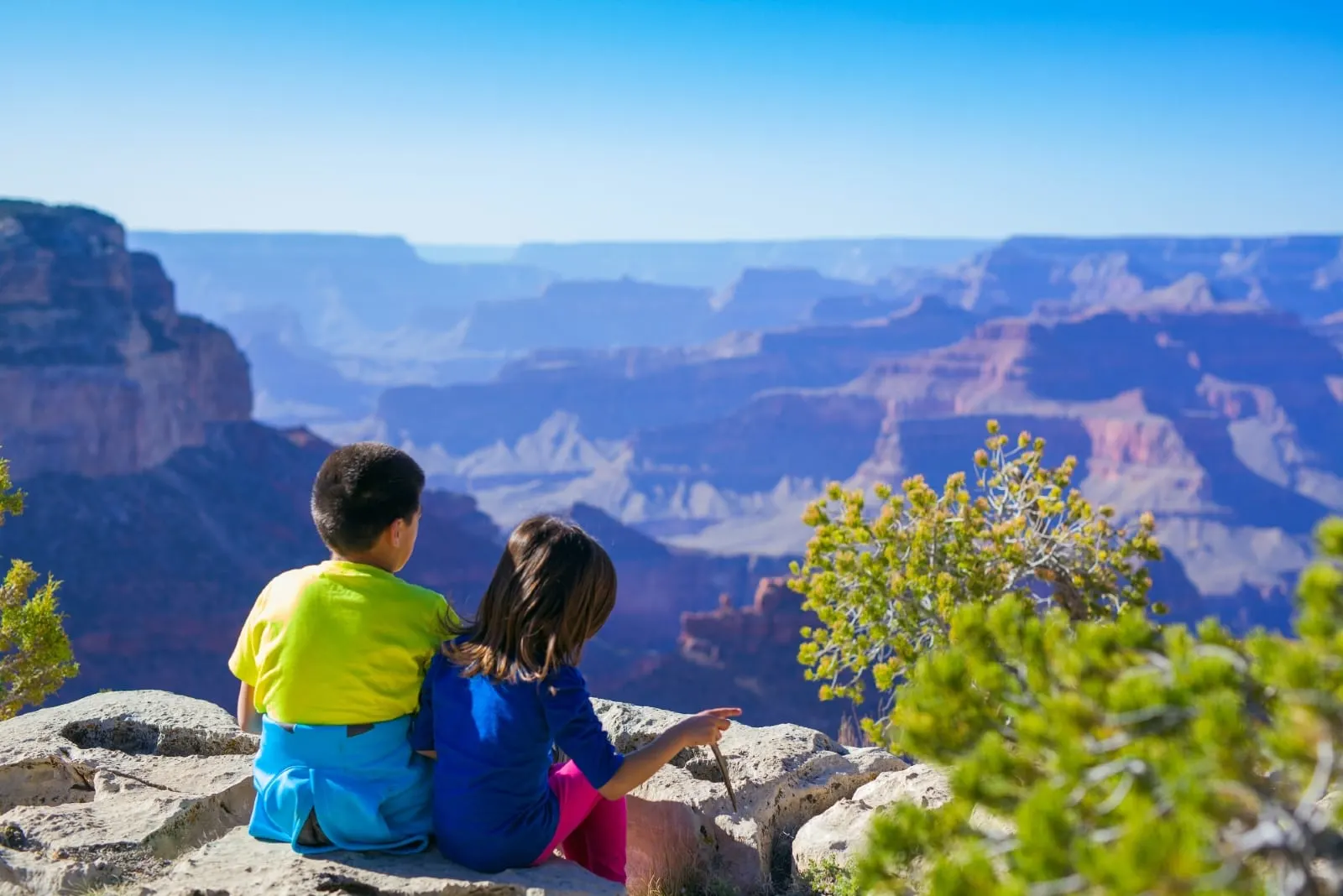 boy and girl sitting on rock looking at mountain