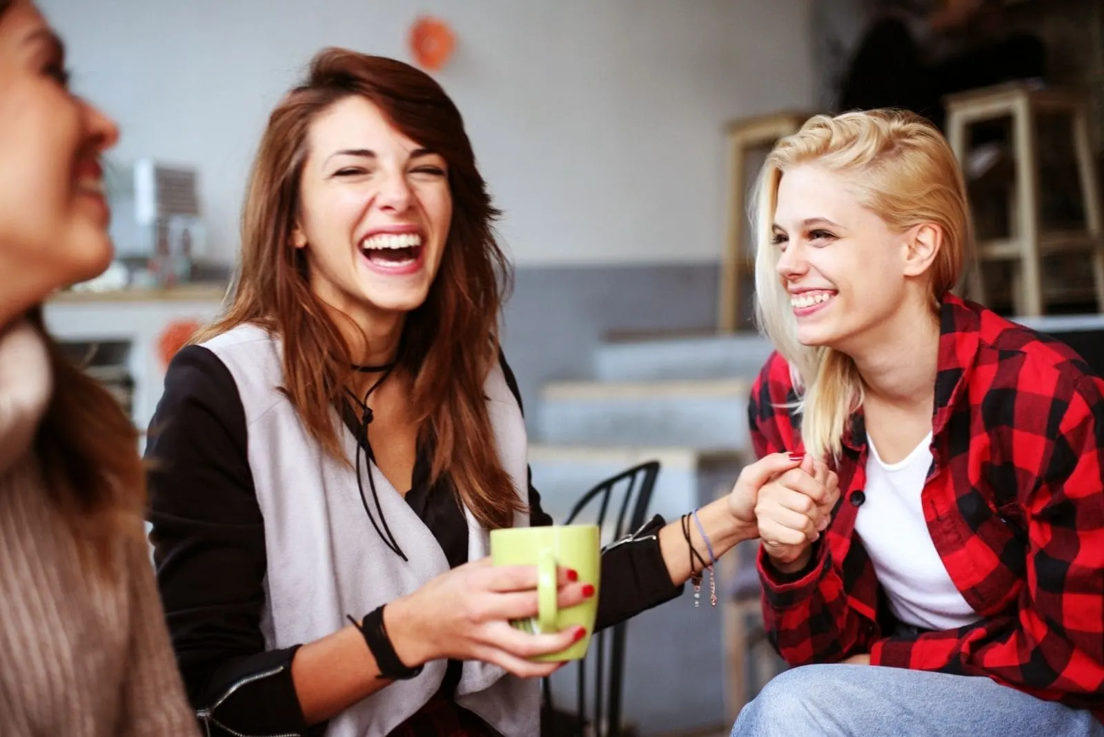 cheerful female friends laughing and drinking coffee at the same time at the cafe/livingroom