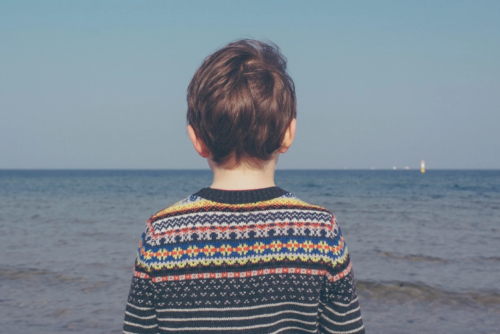 child in multicolored sweater looking at sea