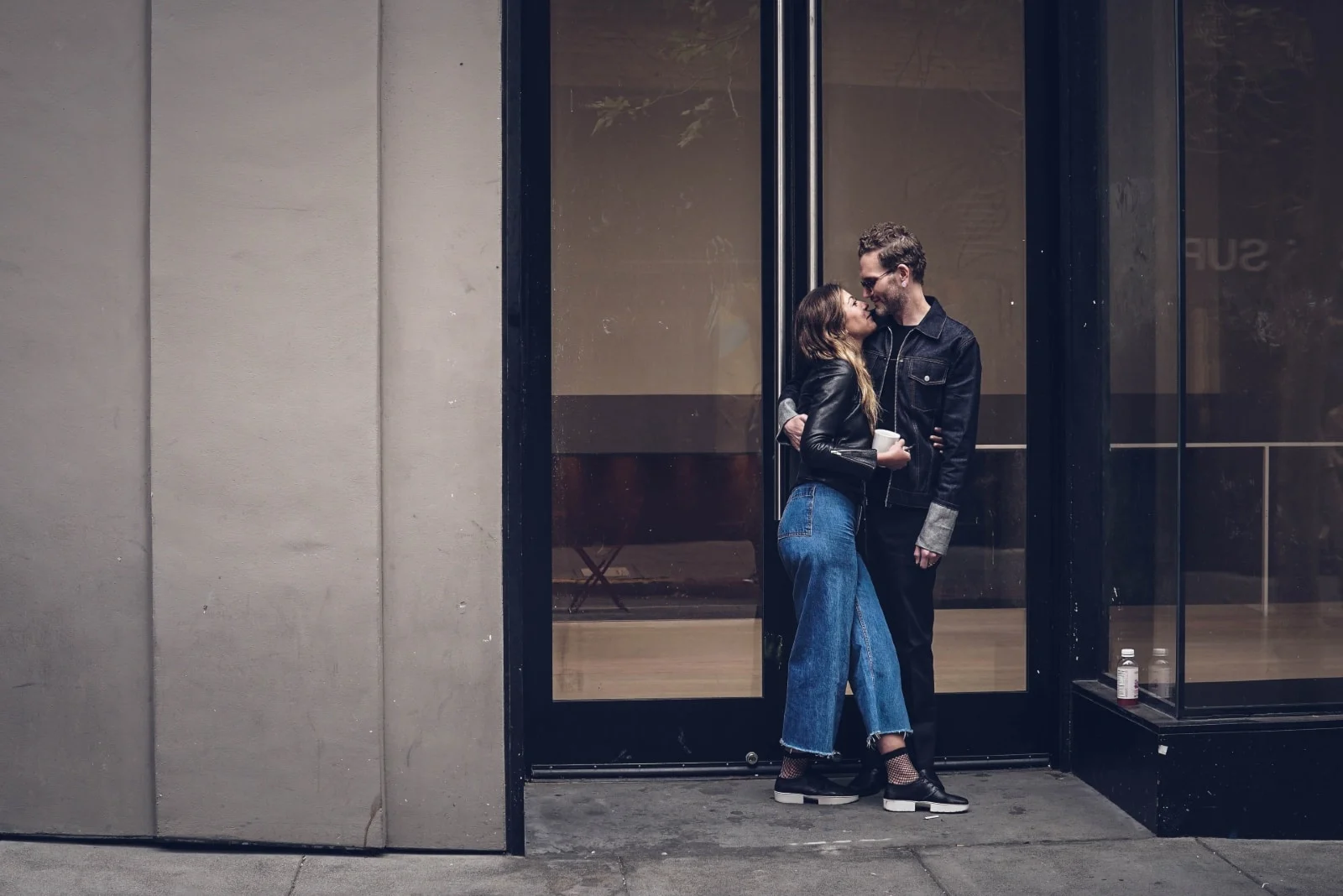 man and woman about to kiss while standing near glass door