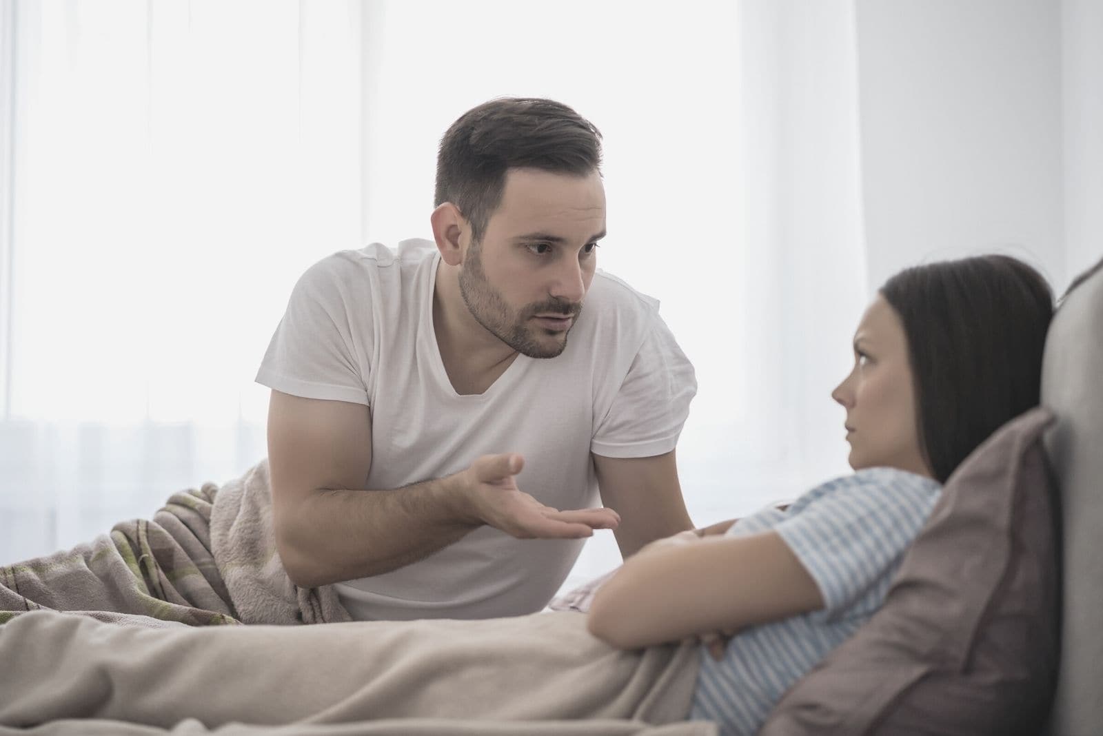 pareja discutiendo en la cama con la mujer enfadada y el hombre dando explicaciones