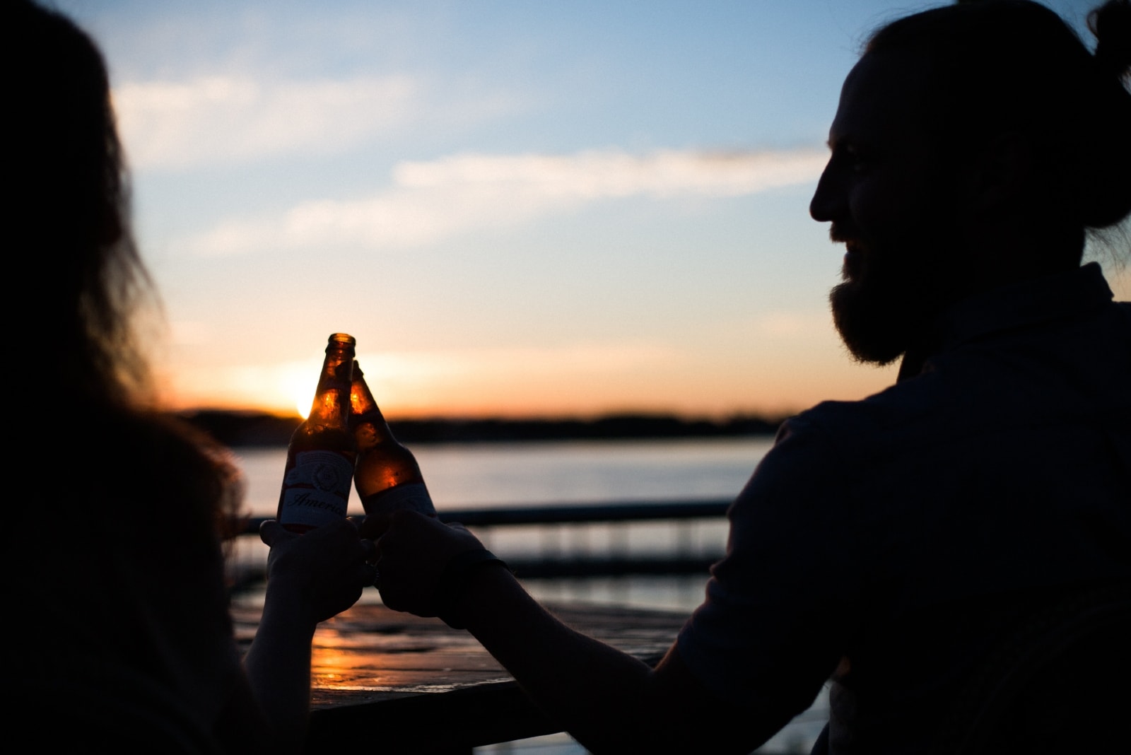 man and woman drinking beer while sitting outdoor