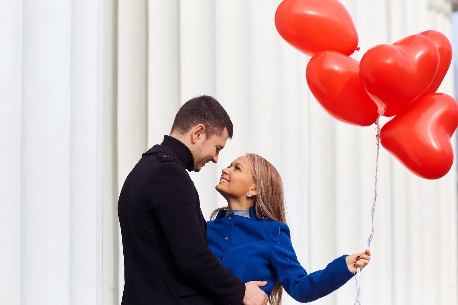 coppia che si abbraccia con palloncini rossi a forma di cuore tenuti dalla donna 