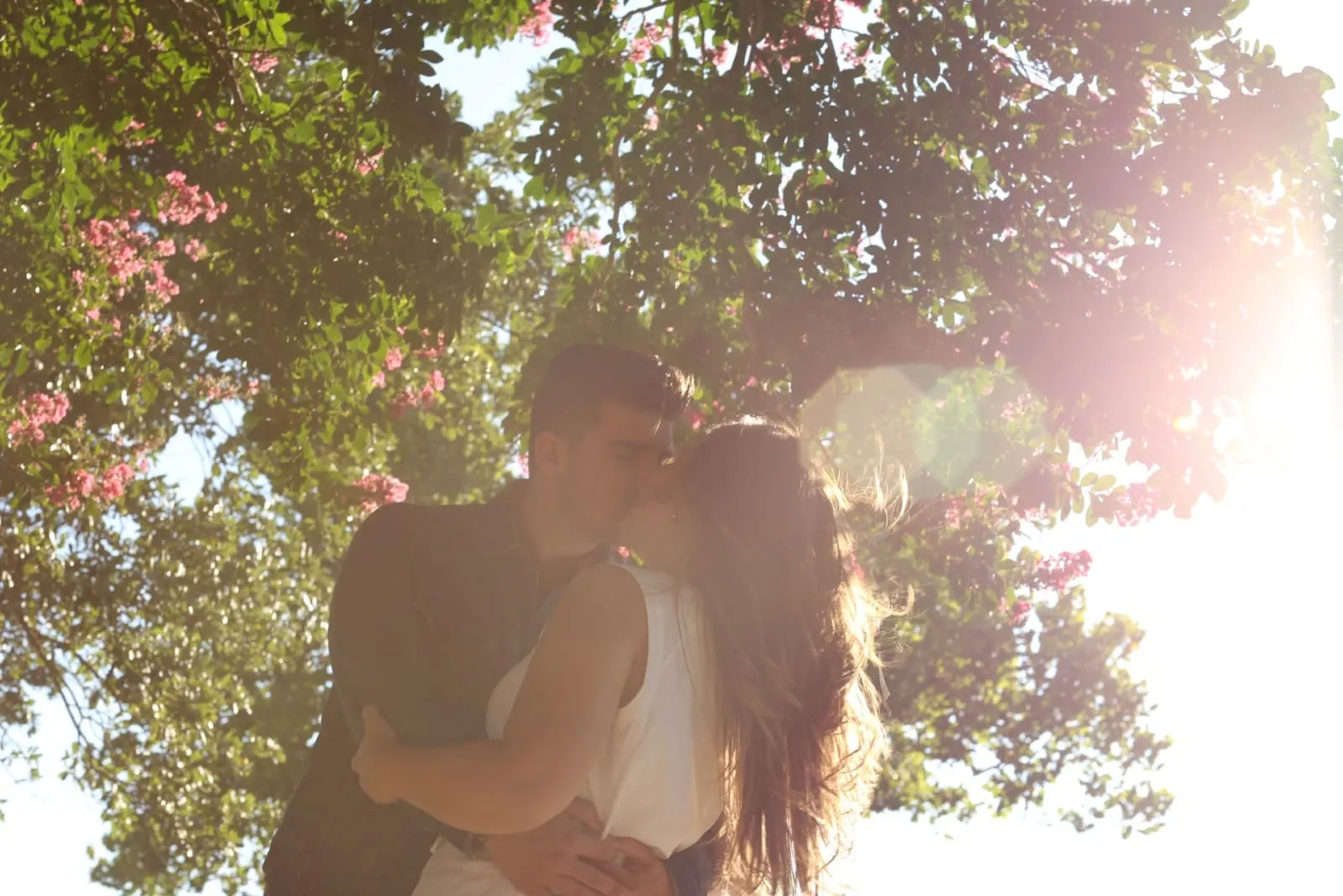 man and woman kissing while standing under the tree