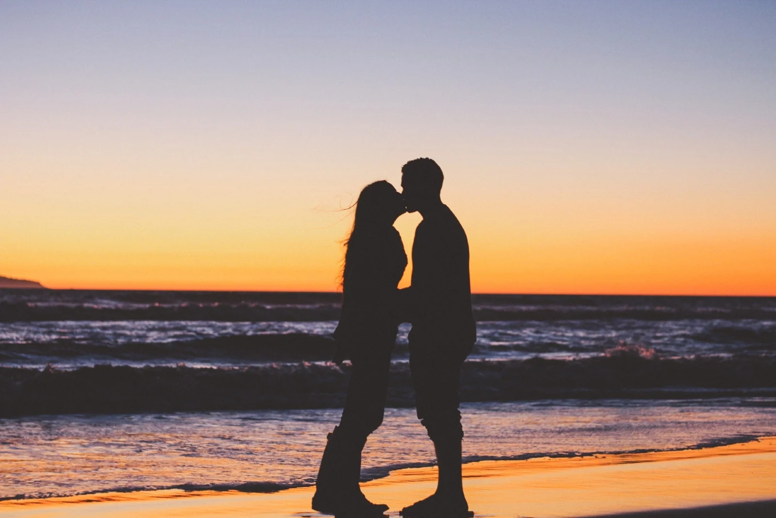 man and woman kissing on beach during sunset