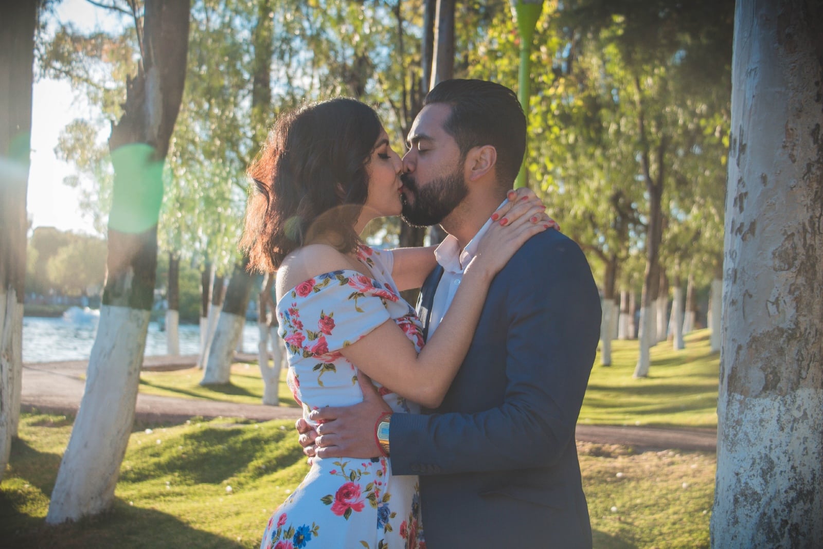 man and woman kissing while standing near tree