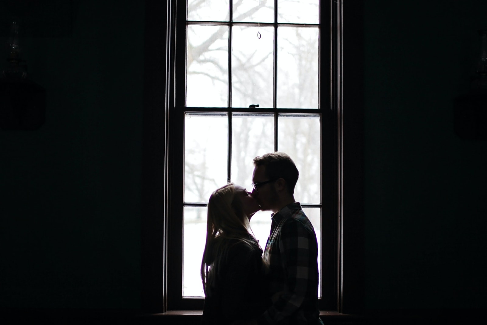 man and woman kissing near window