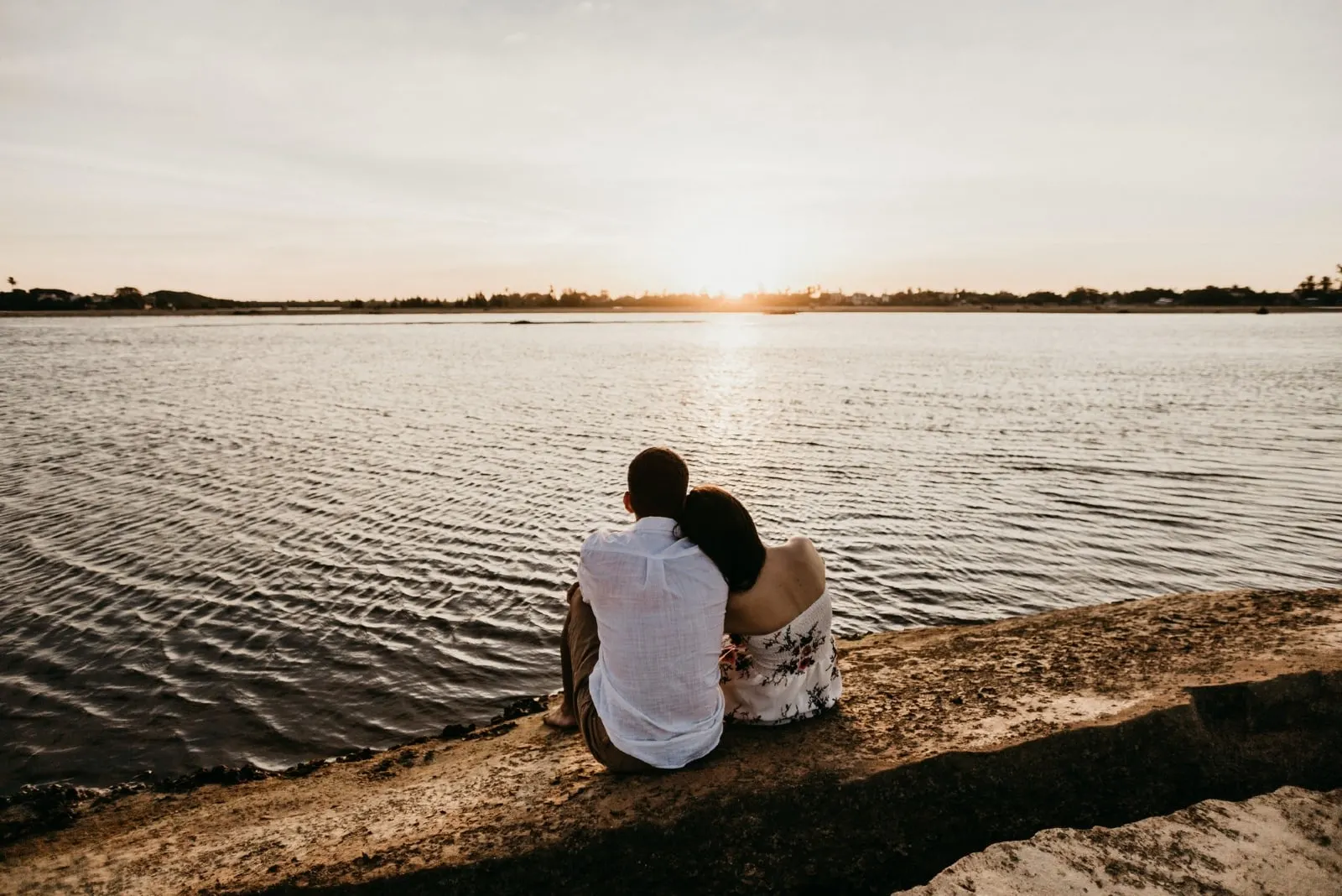 man and woman sitting near water during sunset