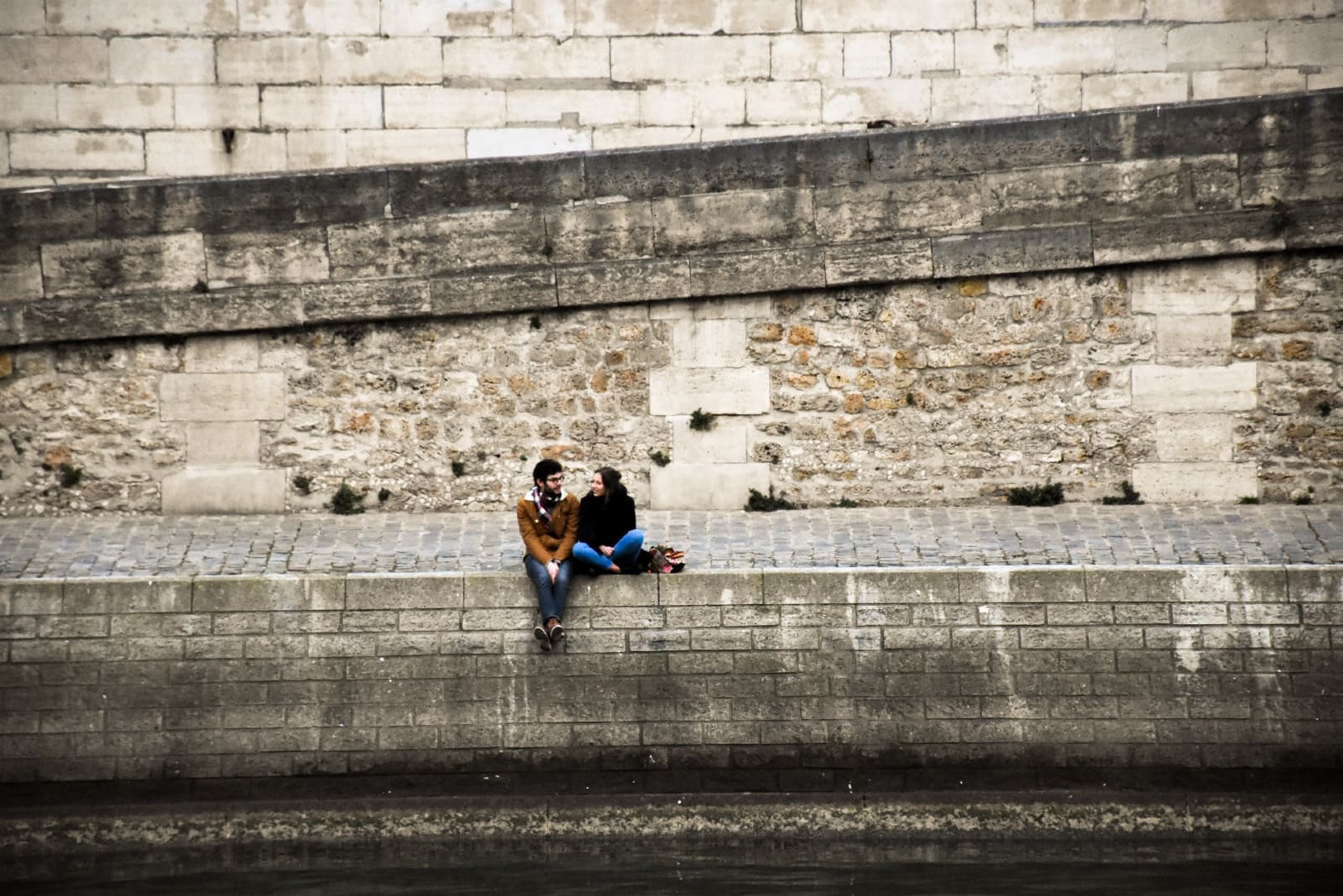 man and woman talking while sitting on concrete surface 