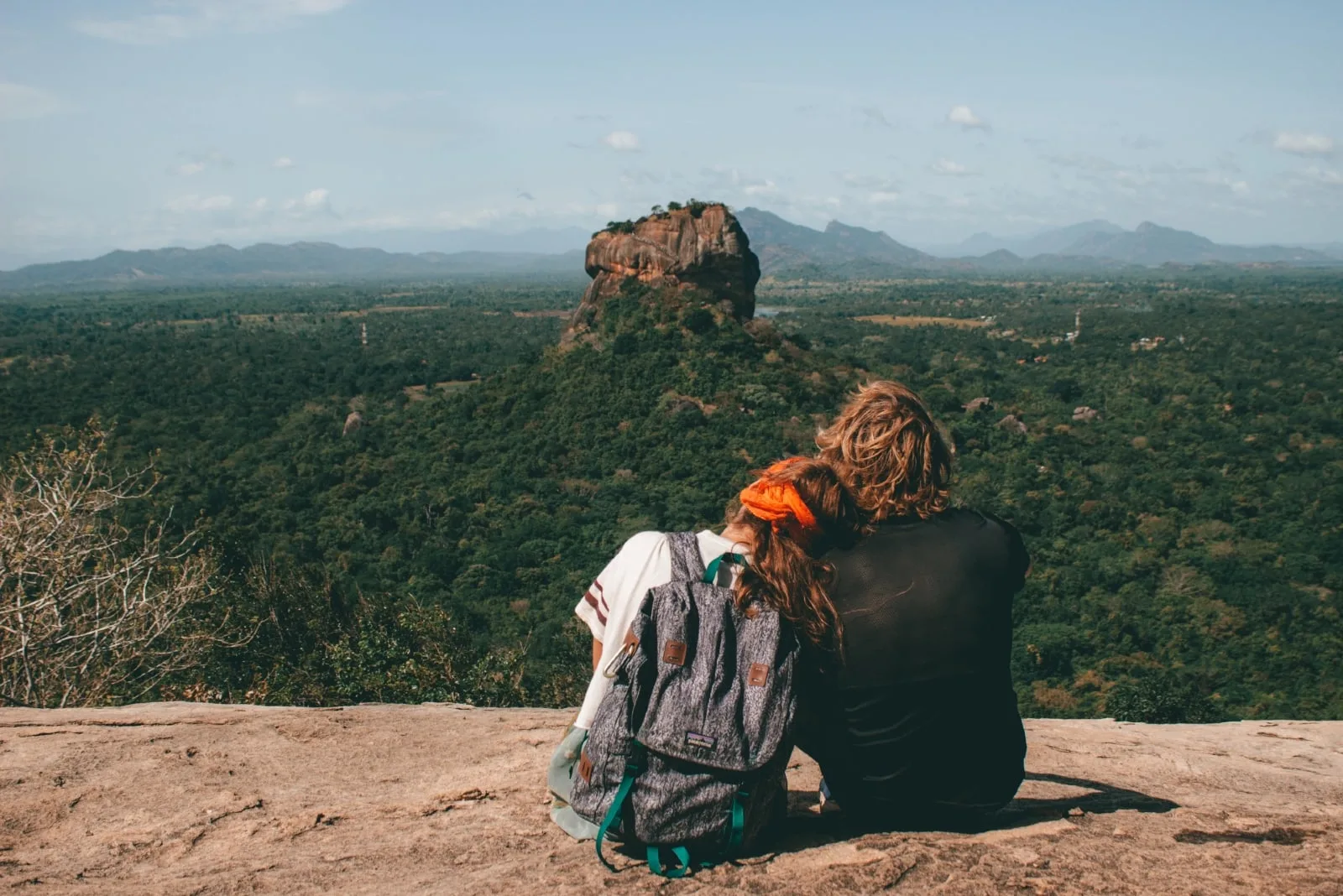 man and woman with backpack sitting on hill