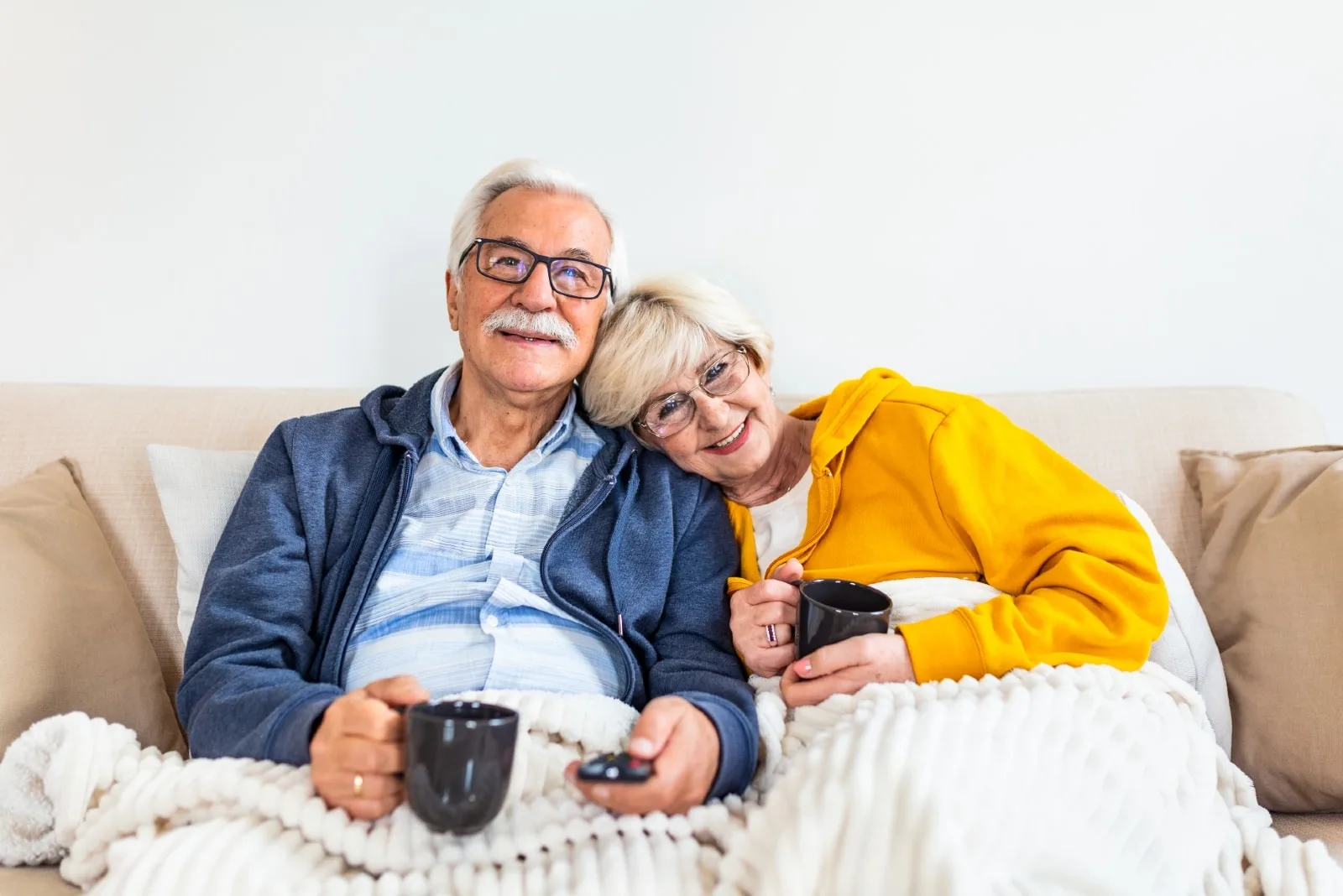 man and woman watching tv while holding black mugs