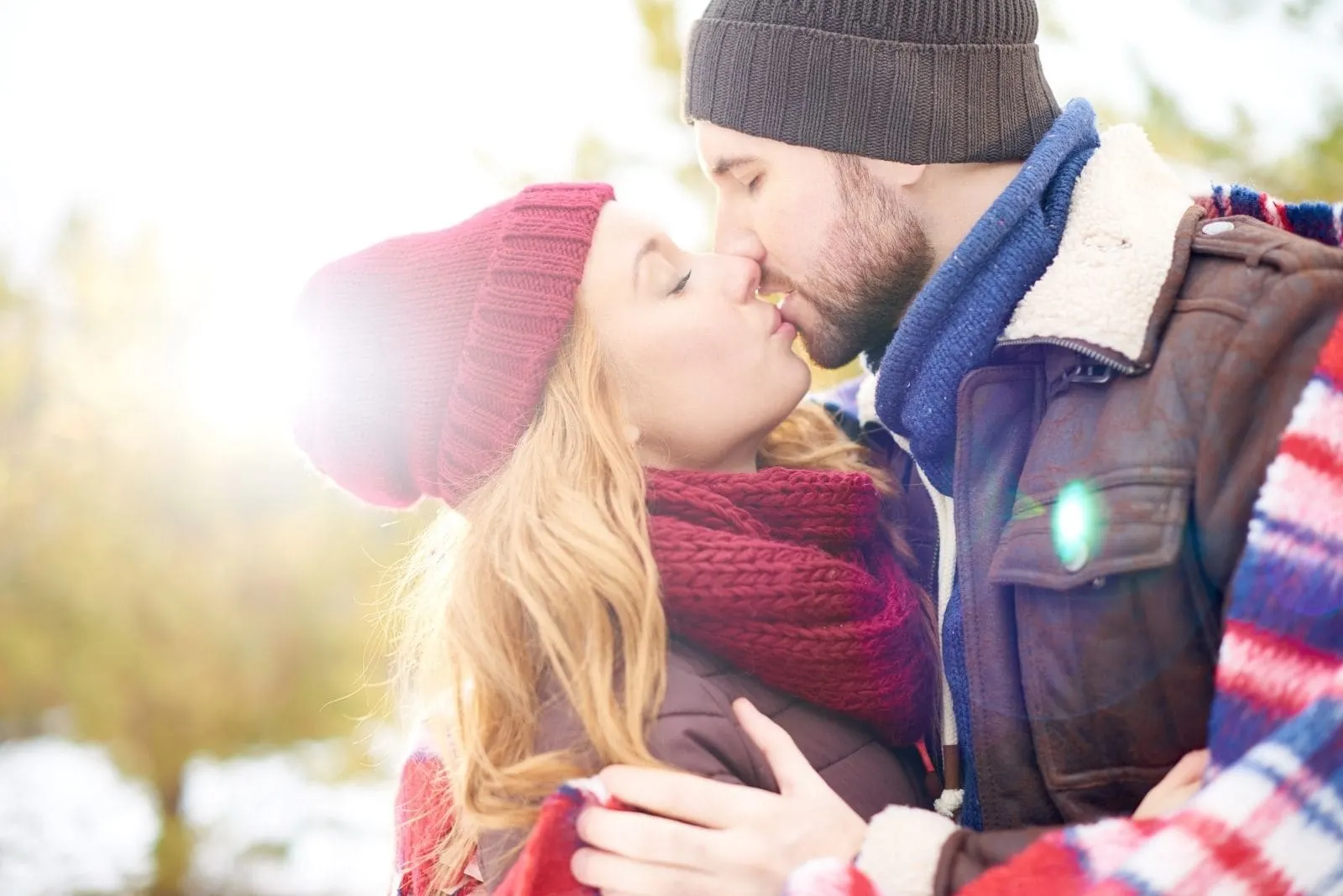 couple wearing winter clothes kissing passionately outdoors