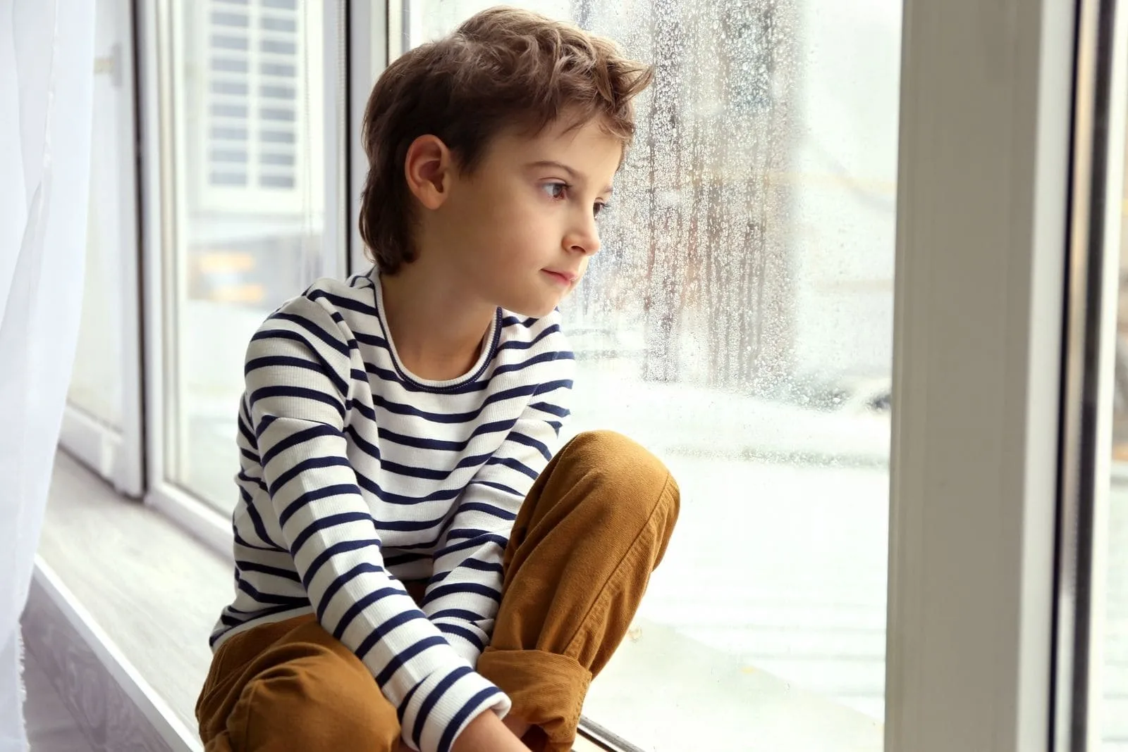 cute little boy sitting by the window sill looking outside