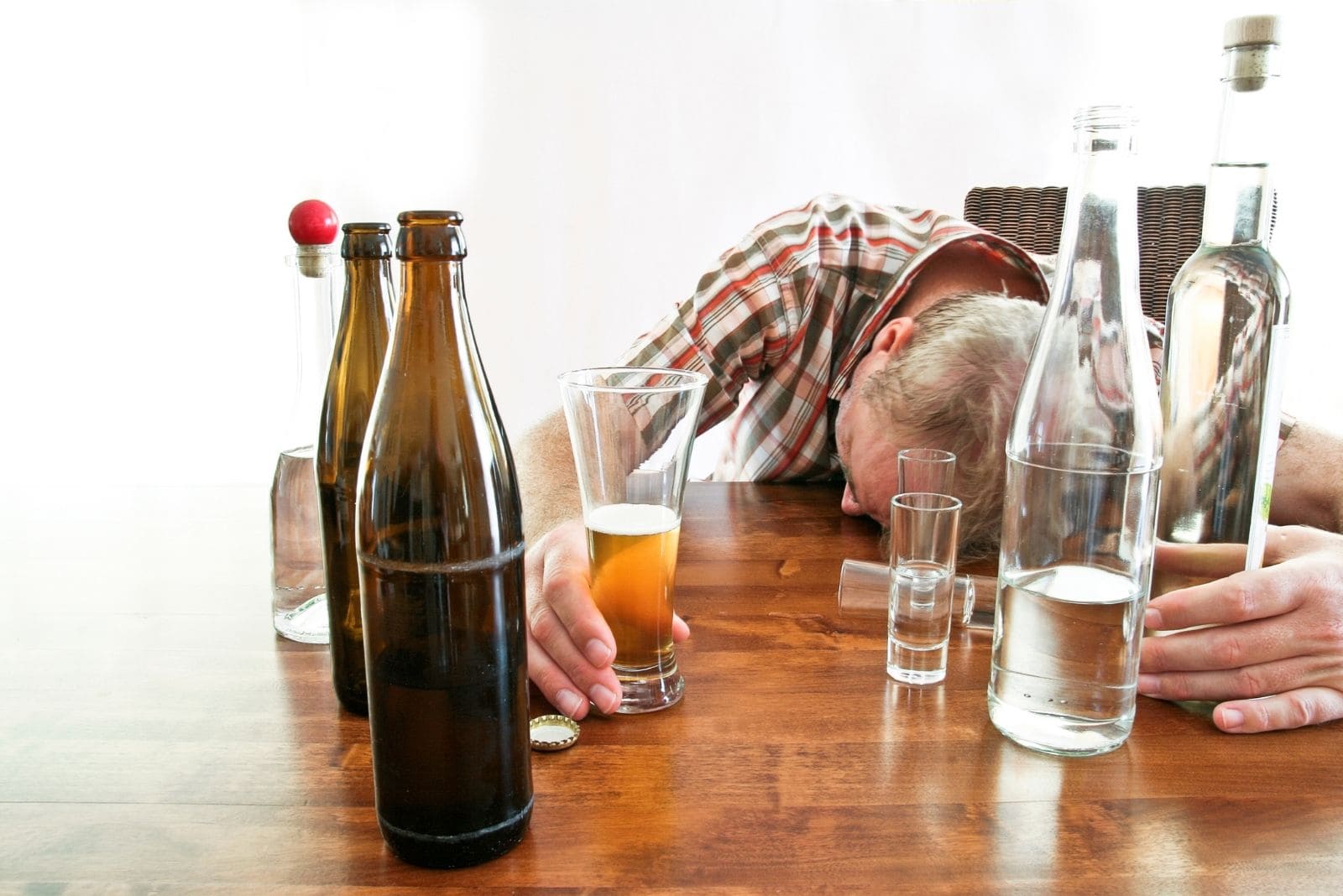 uomo ubriaco che dorme sul tavolo con diverse bottiglie di alcolici e un bicchiere