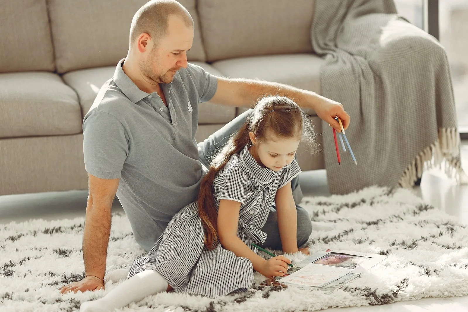 father holding colored pencils while sitting near daughter on carpet