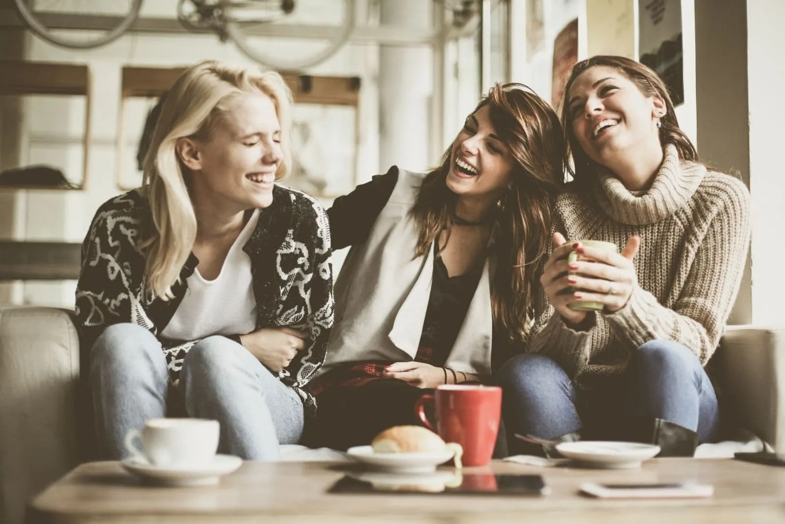 group of friends laughing cheerfully sitting in the couch and having coffee inside the living room