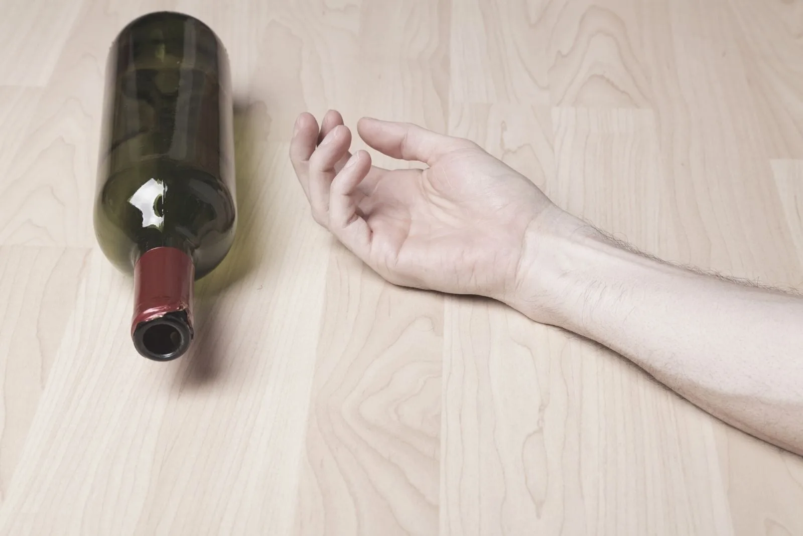 hand of a man on the floor next to an empty bottle