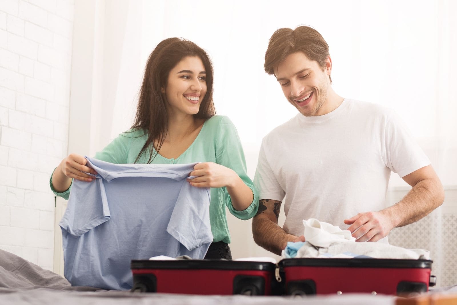coppia felice che ripiega i vestiti nelle valigie per prepararsi a una gita[