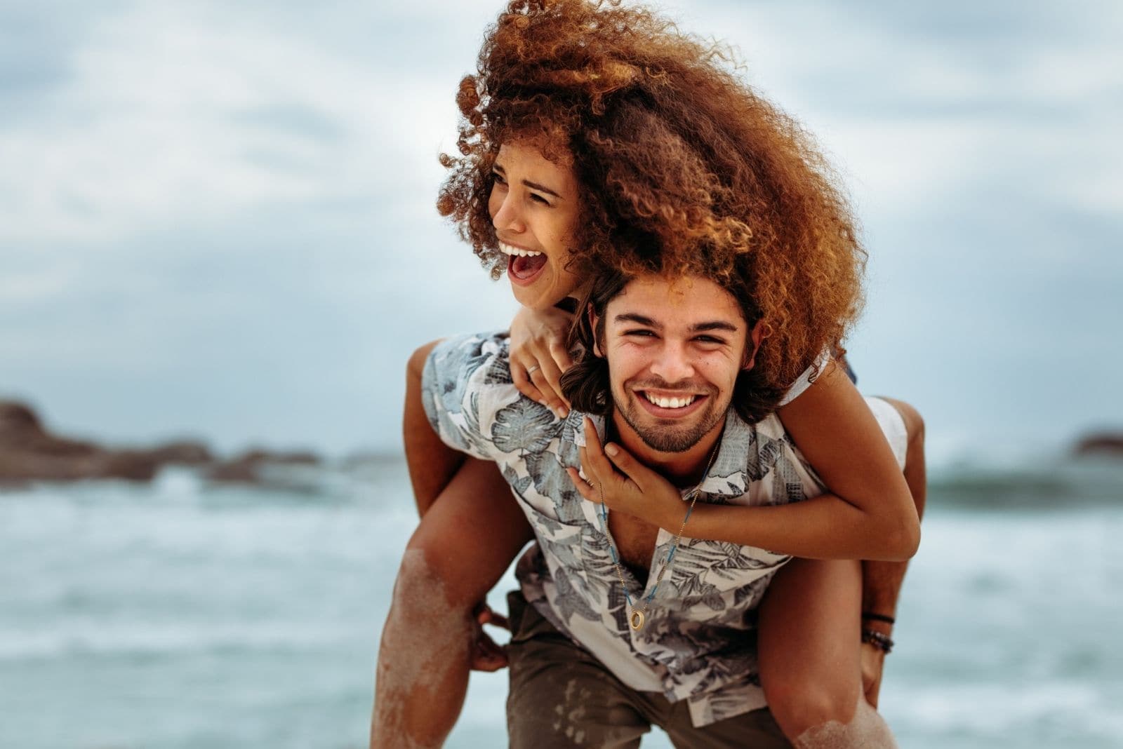 happy couple piggybacking and laughing in the beach