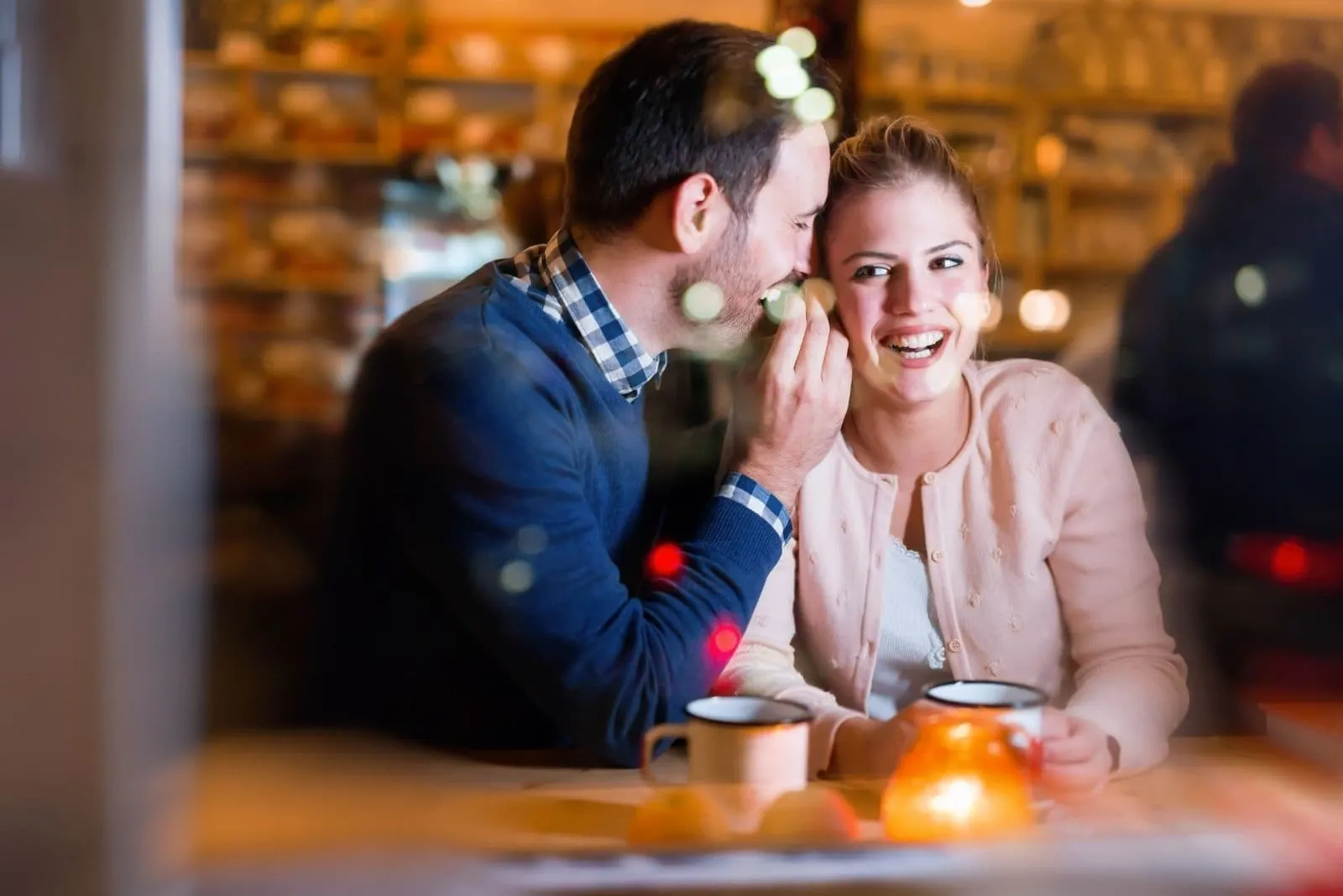 happy man whispering on the woman's ear while dating in a restaurant