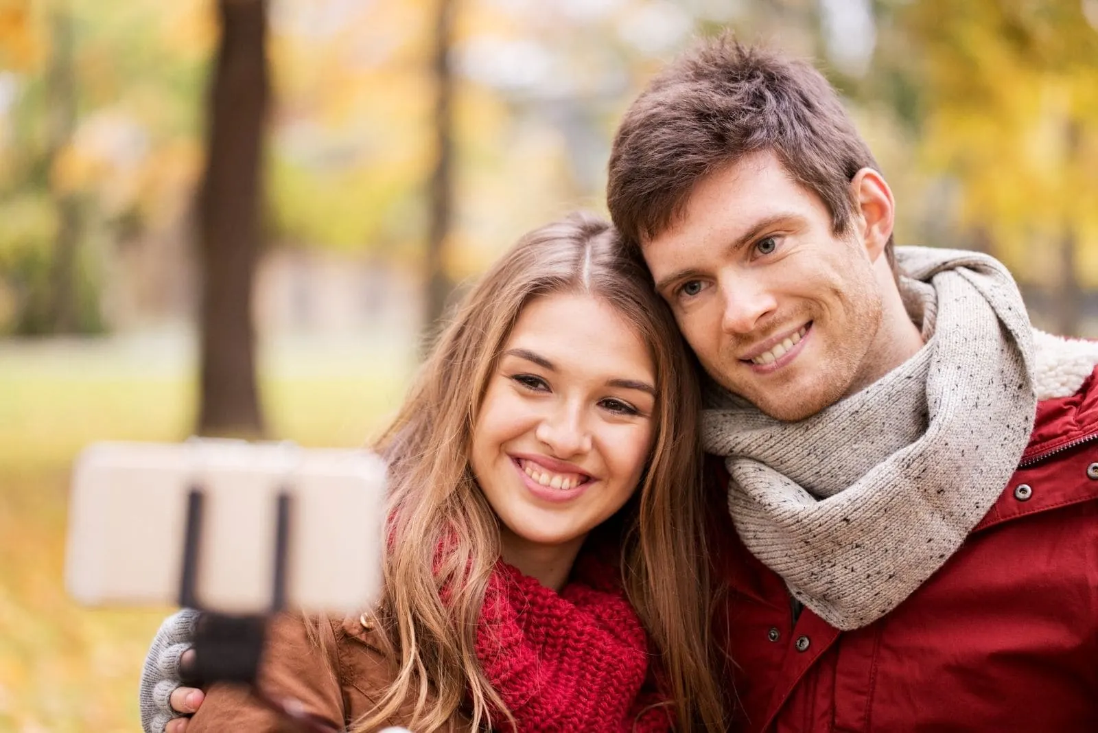 happy smiling couple taking a picture with smartphone and selfie stick during autumn season