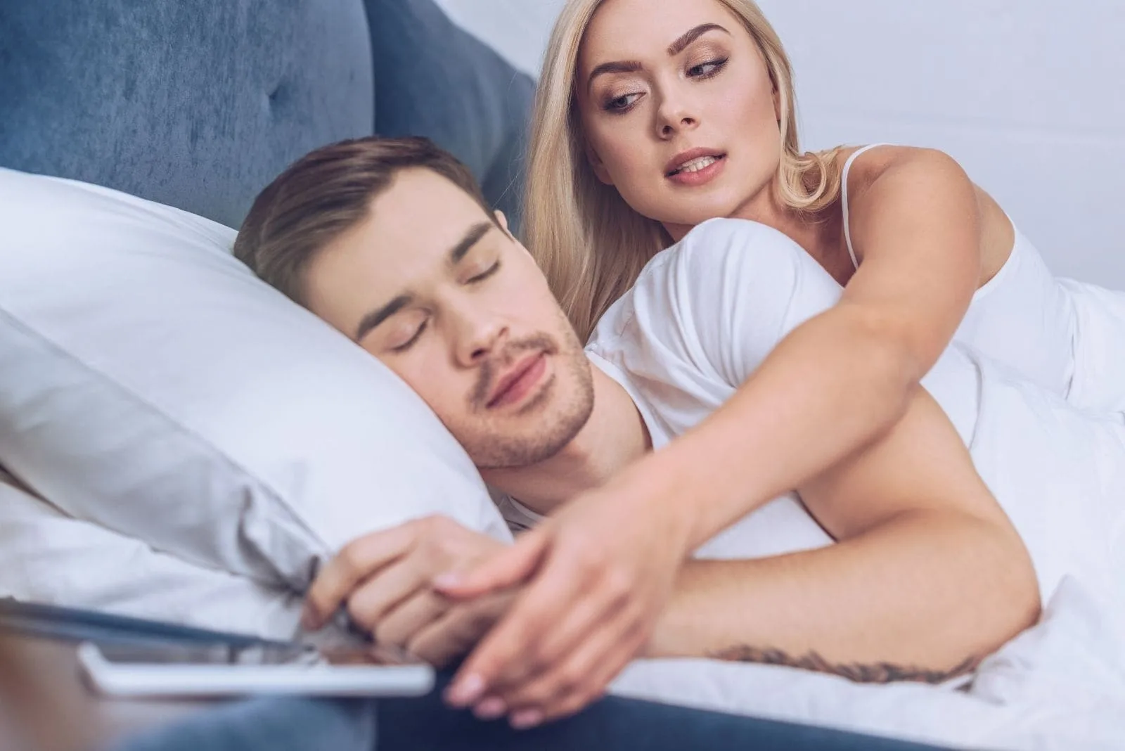 jealous woman snooping over to his boyfriend's cellphone while sleeping on bed